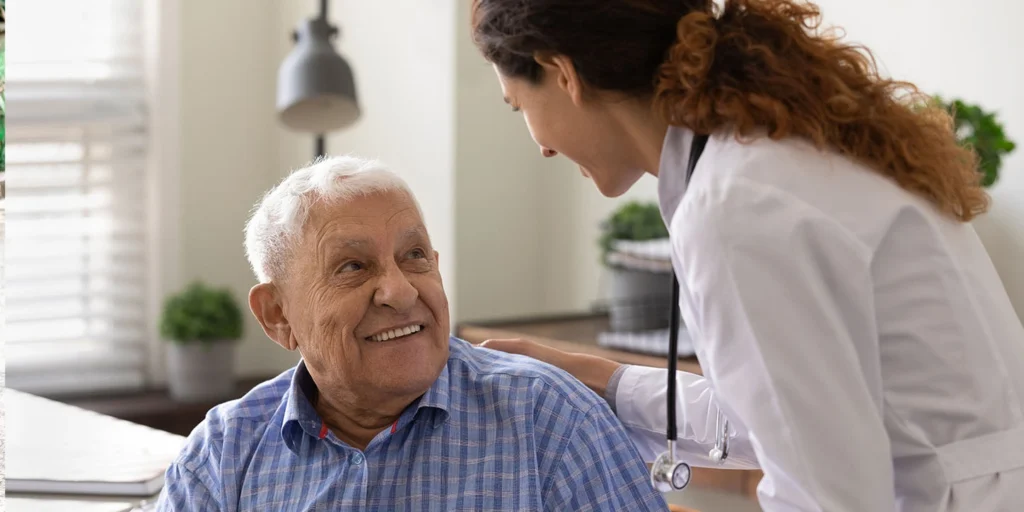 Médica sorridente acolhendo um paciente idoso em consultório durante uma consulta de acompanhamento para Hidrocefalia de Pressão Normal.