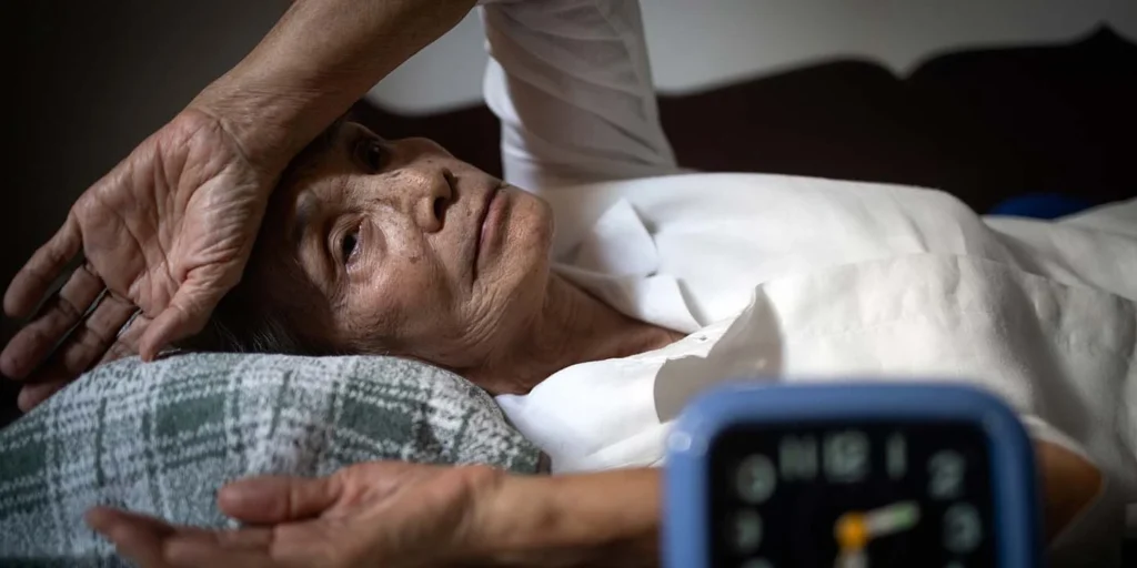 Ideitada na cama exausta, simbolizando a fadiga e os distúrbios do sono comuns na Atrofia de Múltiplos Sistemas (MSA).