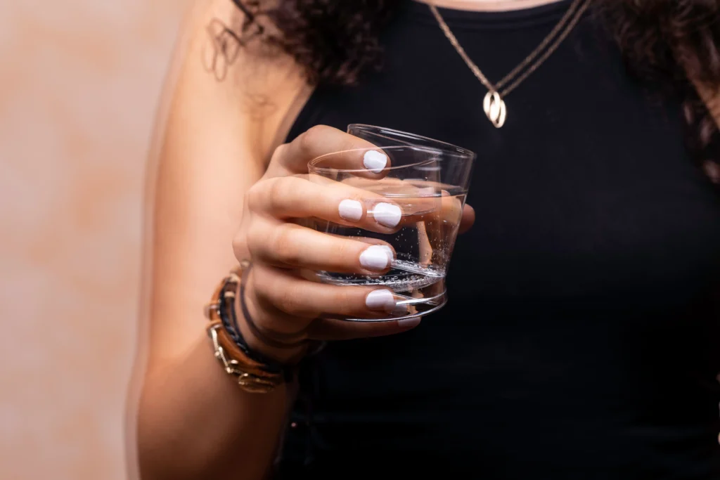 Mão feminina segurando copo de água. A imagem simula o tremor em repouso, sintoma comum no Parkinsonismo Juvenil.