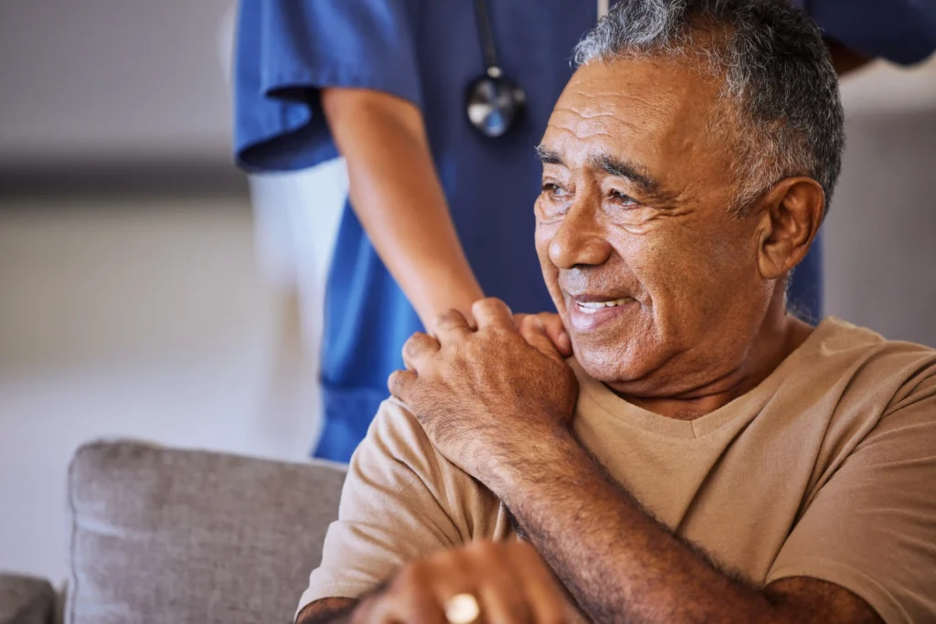 Cuidadora apoia a mão no ombro de um senhor idoso sorrindo, ilustrando os direitos do paciente com Parkinson ao bem-estar.